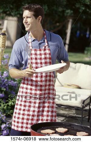 Stock Photo - Man standing with a plate in front of a barbecue grill. Fotosearch