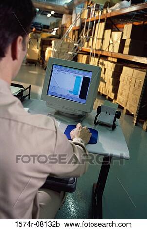 Stock Image - Man working on a computer in a warehouse. Fotosearch