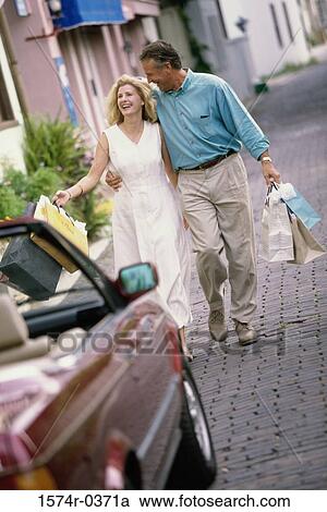 Stock Image - Mature couple walking together holding shopping bags. Fotosearch
