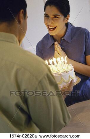 Mid adult man holding a birthday cake in front of a mid adult woman View Large Photo Image Stock Image - Mid adult man holding a birthday cake in front of a mid adult woman. Fotosearch