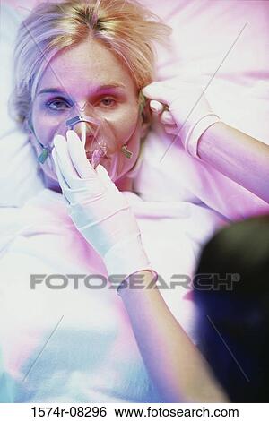 Mid adult woman lying down with a person holding an oxygen mask over her face View Large Photo Image Stock Photograph - Mid adult woman lying down with a person holding an oxygen mask over her face. Fotosearch