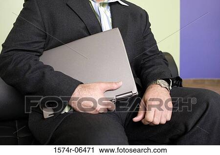 Stock Image - Mid section view of a businessman holding a laptop in an office. Fotosearch