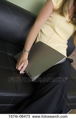 Stock Image - Mid section view of a businesswoman sitting on a couch with a laptop in an office. Fotosearch