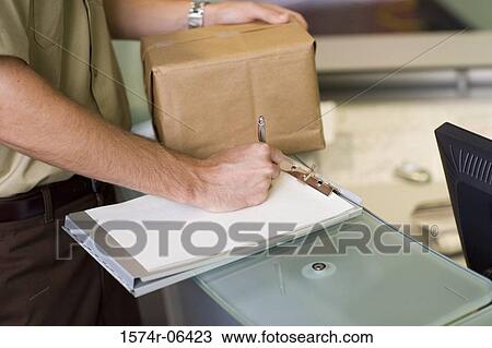 Stock Image - Mid section view of a man holding a box writing on a sheet of paper. Fotosearch