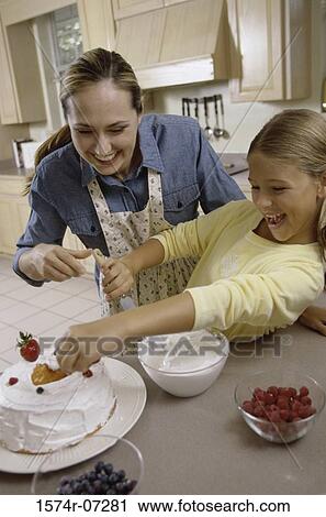 Stock Image - Mother and daughter icing a cake together. Fotosearch