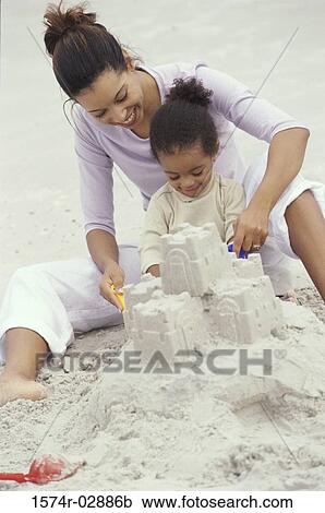 Stock Image - Mother and her daughter making a sand castle on the beach. Fotosearch