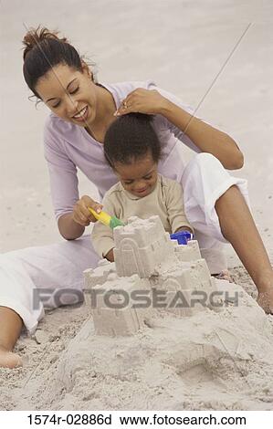 Stock Image - Mother and her daughter making a sand castle on the beach. Fotosearch