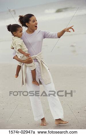 Mother carrying her daughter on the beach View Large Photo Image Stock Image - Mother carrying her daughter on the beach. Fotosearch