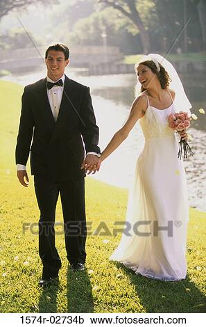 Newlywed couple holding hands and walking by a lake View Large Photo Image Stock Image - Newlywed couple holding hands and walking by a lake. Fotosearch