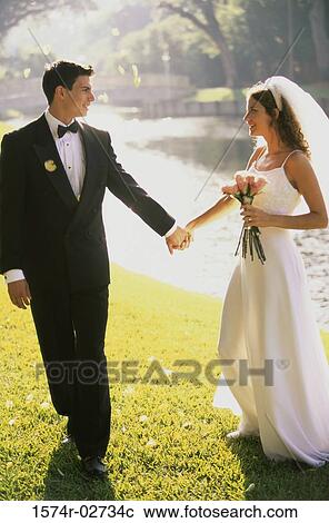 Newlywed couple holding hands and walking by a lake View Large Photo Image Stock Image - Newlywed couple holding hands and walking by a lake. Fotosearch