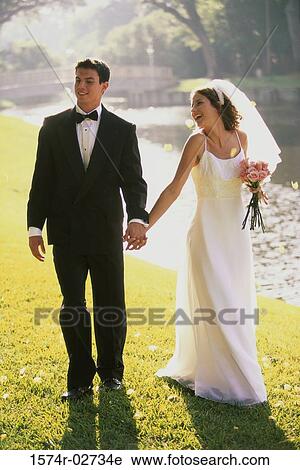 Newlywed couple holding hands and walking by a lake View Large Photo Image Stock Image - Newlywed couple holding hands and walking by a lake. Fotosearch