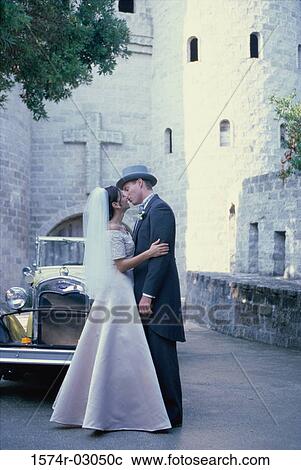 Newlywed couple kissing each other in front of an antique car View Large Photo Image Stock Image - Newlywed couple kissing each other in front of an antique car. Fotosearch