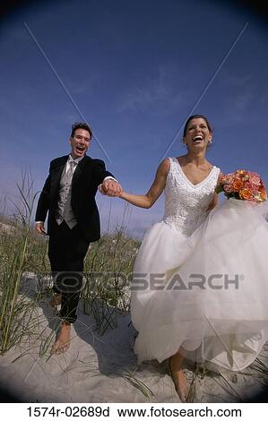 Stock Image - Newlywed couple running on sand. Fotosearch