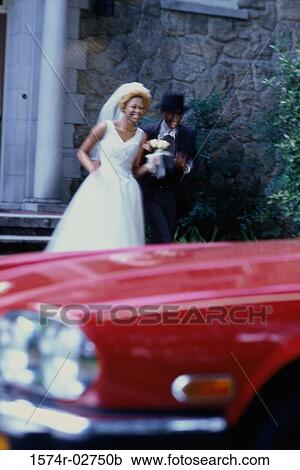 Stock Image - Newlywed couple running towards a car. Fotosearch
