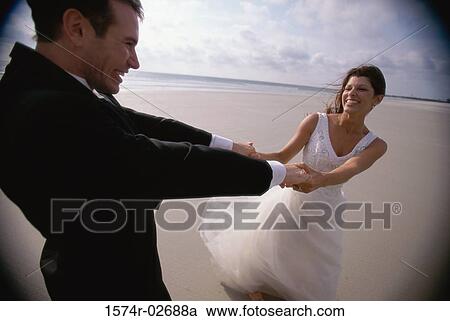 Stock Image - Newlywed couple spinning each other on the beach. Fotosearch