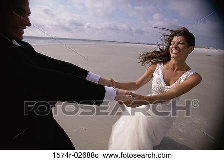Stock Image - Newlywed couple spinning each other on the beach. Fotosearch