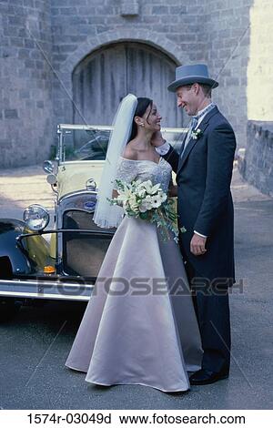 Stock Image - Newlywed couple standing in front of an antique car. Fotosearch