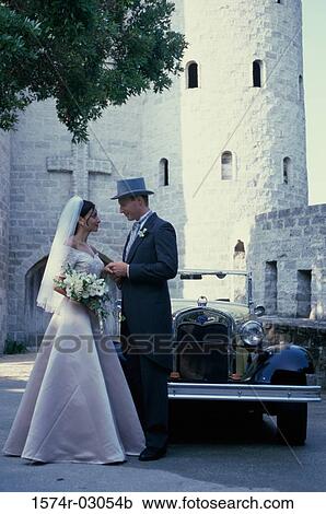 Stock Image - Newlywed couple standing in front of an antique car. Fotosearch