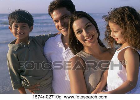 Stock Image - Parents holding their son and daughter on the beach. Fotosearch