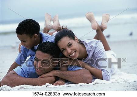 Stock Image - Parents lying with their son on the beach. Fotosearch