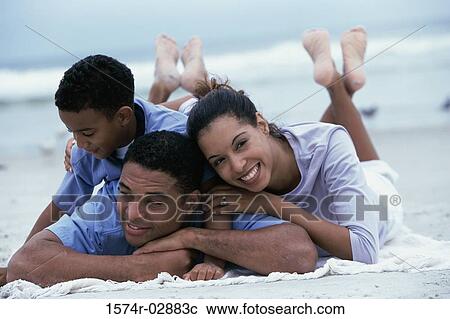Stock Image - Parents lying with their son on the beach. Fotosearch