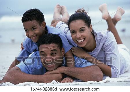 Stock Image - Parents lying with their son on the beach. Fotosearch