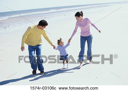 Stock Image - Parents playing with their daughter on the beach. Fotosearch