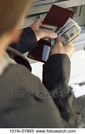 Stock Image - Person putting cash into his wallet in front of an ATM. Fotosearch