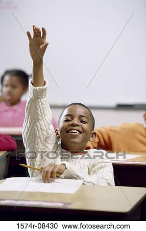 Stock Image - Portrait of a boy raising his hand in class. Fotosearch
