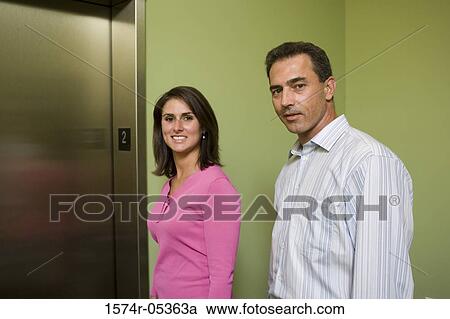 Stock Image - Portrait of a businessman and a businesswoman standing near an elevator. Fotosearch