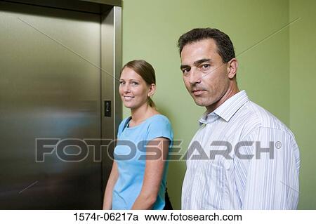 Stock Image - Portrait of a businessman and a businesswoman standing near an elevator. Fotosearch