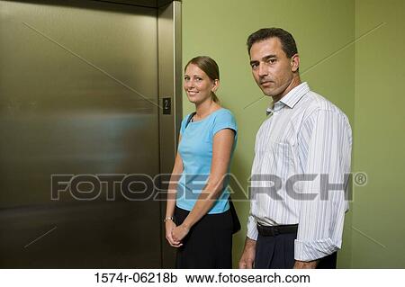 Stock Image - Portrait of a businessman and a businesswoman standing near an elevator. Fotosearch