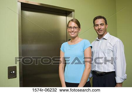 Stock Image - Portrait of a businessman and a businesswoman standing near an elevator. Fotosearch
