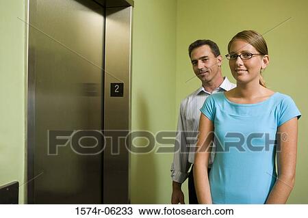 Stock Image - Portrait of a businessman and a businesswoman standing near an elevator. Fotosearch