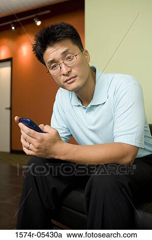 Stock Image - Portrait of a businessman holding a mobile phone in an office. Fotosearch