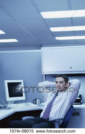 Stock Photography - Portrait of a businessman seated at an office desk with his hands behind his head. Fotosearch