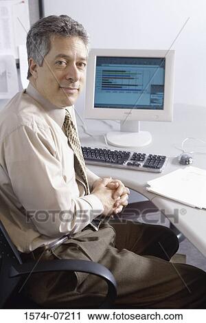 Stock Image - Portrait of a businessman seated in front of a computer. Fotosearch