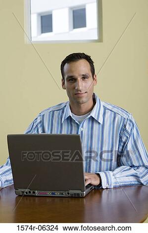 Portrait of a businessman sitting in front of a laptop in an office View Large Photo Image Picture - Portrait of a businessman sitting in front of a laptop in an office. Fotosearch