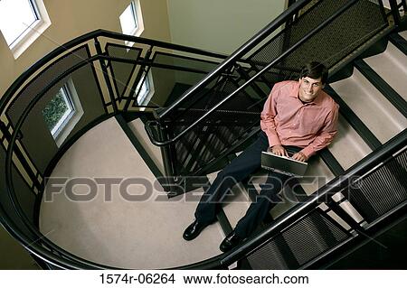 Portrait of a businessman sitting on a staircase working on a laptop View Large Photo Image Picture - Portrait of a businessman sitting on a staircase working on a laptop. Fotosearch