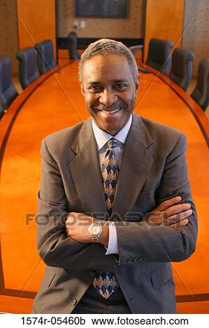 Stock Image - Portrait of a businessman standing in a conference room smiling. Fotosearch
