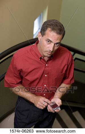 Stock Image - Portrait of a businessman standing on a staircase holding a mobile phone. Fotosearch