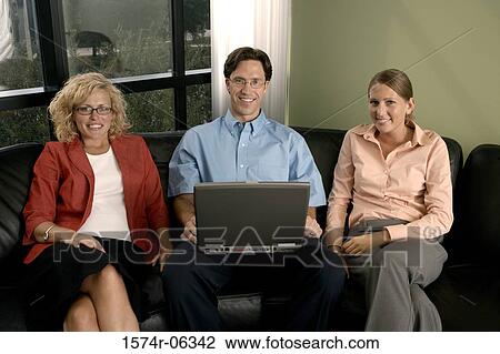 Portrait of a businessman using a laptop with two businesswomen sitting beside him View Large Photo Image Stock Image - Portrait of a businessman using a laptop with two businesswomen sitting beside him. Fotosearch