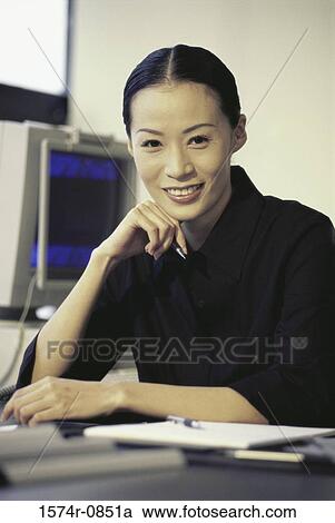 Stock Image - Portrait of a businesswoman sitting at a desk smiling. Fotosearch