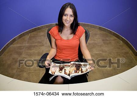 Picture - Portrait of a businesswoman sitting in a chair reading a magazine in an office. Fotosearch
