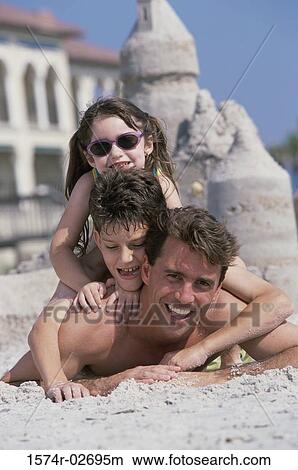 Portrait of a father lying on the beach with his son and daughter View Large Photo Image Picture - Portrait of a father lying on the beach with his son and daughter. Fotosearch