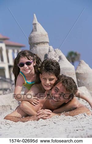 Stock Image - Portrait of a father lying on the beach with his son and daughter. Fotosearch