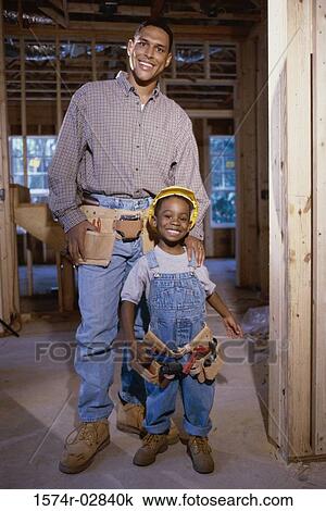 Stock Image - Portrait of a father standing with his son at a construction site. Fotosearch