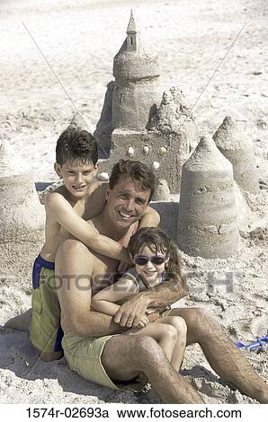 Stock Image - Portrait of a father with his son and daughter sitting on the beach. Fotosearch