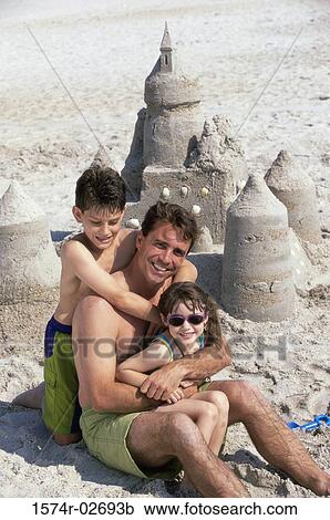 Stock Image - Portrait of a father with his son and daughter sitting on the beach. Fotosearch