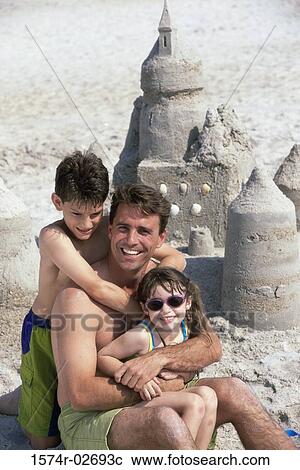 Stock Image - Portrait of a father with his son and daughter sitting on the beach. Fotosearch